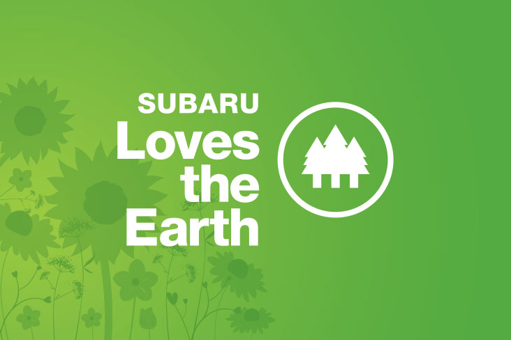 Subaru Loves the Earth logo with white lettering on a green background. To the right of the words “Subaru Loves the Earth” is an illustration of three evergreen trees enclosed in a circle.