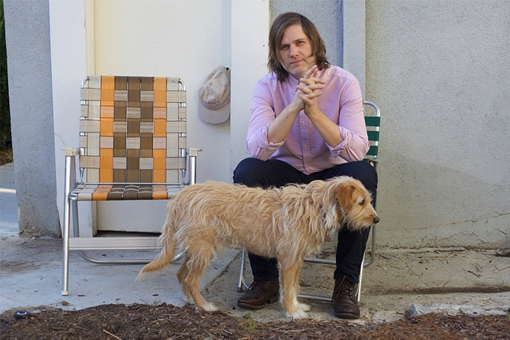 Eric Johnson of Fruit Bats sitting in a folding chair with a dog at his feet.