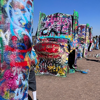 Close-up view of several buried Cadillacs at the Cadillac Ranch. They are spray painted in many colors and are pointing up toward the blue sky.