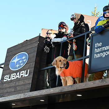 Subaru WinterFest participants and a geared-up golden retriever stand on a deck.