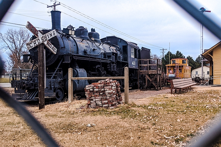 A large black steam locomotive with a railroad crossing sign in front of it at the Trails & Rails Museum.