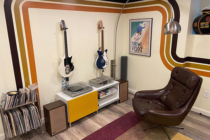 A view of writer Craig Fitzgerald's basement room showing two electric guitars on the wall, vinyl record albums in a rack, a brown leather chair, and a complete record player setup, including the Sony STR-VX250, which was his first receiver, the Technics SL-Q300 turntable and KLH speakers from Facebook Marketplace.