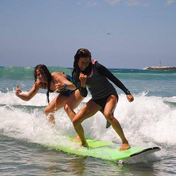 two surfing students catching a wave into shore sharing a surfboard