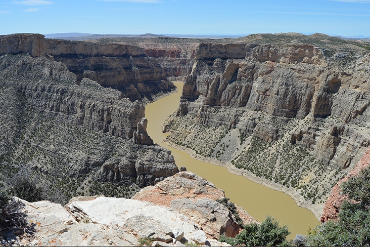 A shot taken of Bighorn Canyon National Recreation Area in Montana that shows a river flowing between two immense dry-looking, rocky canyons.
