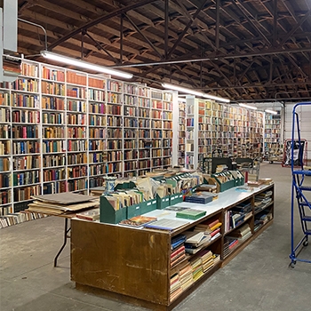 Interior view of Booked Up, with books from floor to ceiling along a back wall and a large tabletop in the center with more. 