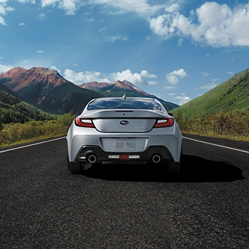 A rear view of the 2022 Subaru BRZ in Ice Silver Metallic on an asphalt road with mountains in the distance and clear, blue skies.