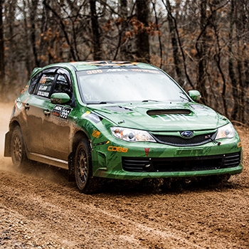 A student takes a green Subaru Impreza for a spin on the muddy track during driving school.