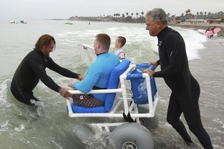Waves of Impact instructors help student into the water in a wheelchair