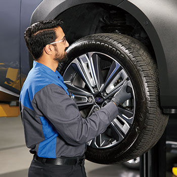 A male mechanic wearing protective glasses is installing a new wheel on a Subaru vehicle.