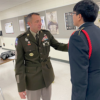 Subaru owner Michael Green is wearing an Army service uniform as he speaks to a high school student in a navy-blue uniform. 
