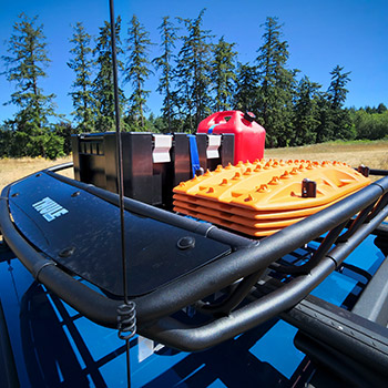 A Genuine Subaru Accessories Thule® roof basket holds four Maxtrax Mini recovery boards, a 5-gallon fuel can, and a Front Runner® Outfitters Wolf Pack Pro box.