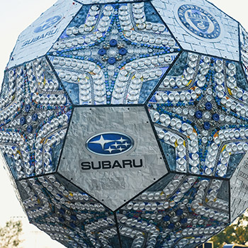 A picture of the zero-landfill sculpture at Subaru Park in Chester, Pennsylvania. It has the Subaru Logo with the Pleiades constellation in the center. The ball is made up repeating designs in blue-colored hexagons.