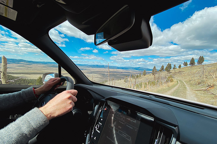 A view taken from the passenger seat shows the author driving with a Montana mountain landscape in the background.