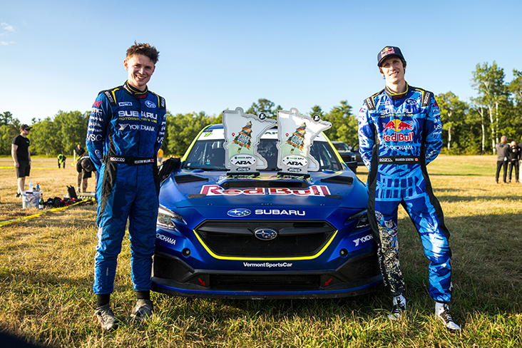 Co-driver Keaton Williams (on the left) and driver Brandon Semenuk (on the right) are wearing racing suits and are standing in front of the all-new WRX rally car; two large Minnesota-shaped trophies adorn the hood.