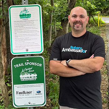 Kyle Williams is standing next to a trail sign for the Capital Area Greenbelt.