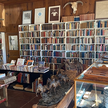 View of a room at Booked up, with a paneled wall in the upper half that is decorated with pictures in frames. Rows of books are below it.