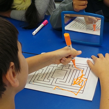 A student trying to complete a maze by looking at it in a mirror. This is a challenge that Walk In My Shoes provides to kids to help them better understand how it may be for students with medical conditions, learning differences and developmental delays.
