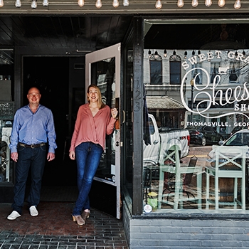 Sweetgrass Dairy storefront with the owners standing out front in the doorway, smiling.