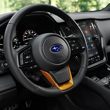 Steering wheel closeup with black leather details and Subaru logo in the center