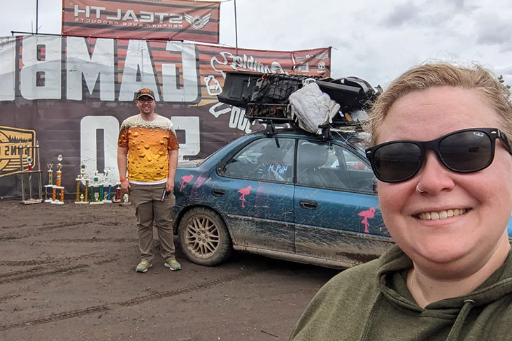 Leslie Boro smiling in front of her Subaru during the Gambler 500. The roof of the blue Subaru is loaded with refuse collected during the event.