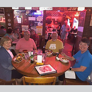 The two married couples are sitting at a table in a restaurant, smiling. It is dim-lit, and they have fresh bowls of chili on the table in front of them.