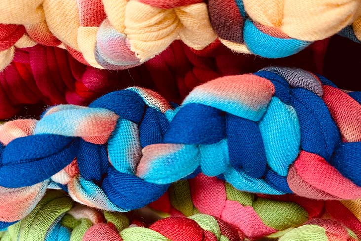 A handmade, braided dog toy in bright colors made of recycled shirts.