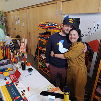 Founders Nick and Kate Bergmann of Peace House Studio are hugging and smiling in the clothing workshop.