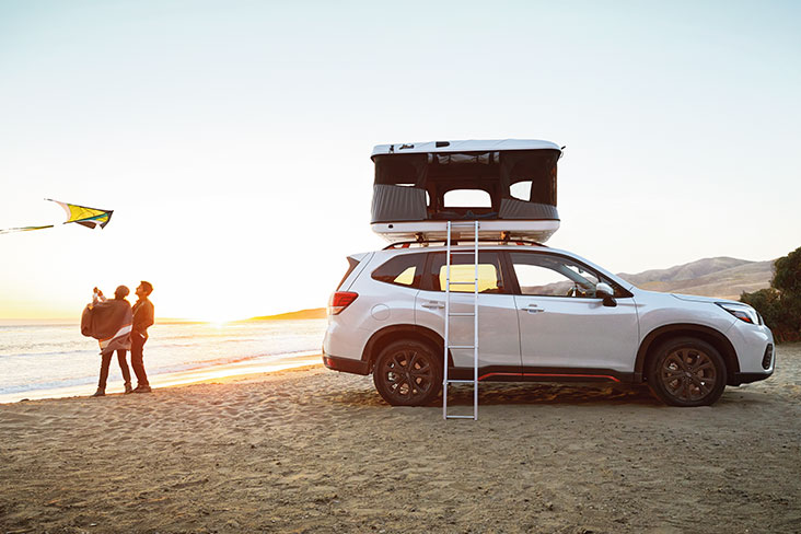 A rooftop tent pitched on top of a Forester Sport on the beach.