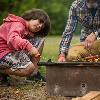 Craig and Harry cooking hot dogs on a campfire