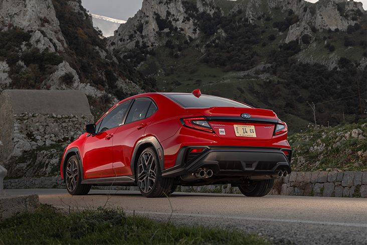 A shiny red Subaru WRX TR seen from behind. It's parked on asphalt and ragged mountains can be seen beyond the vehicle.