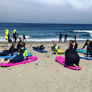 surf instructor demonstrates surfing on dry land to group of students