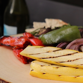 A closeup of sliced, grilled red and green peppers, other vegetables, crackers and a bottle of wine.