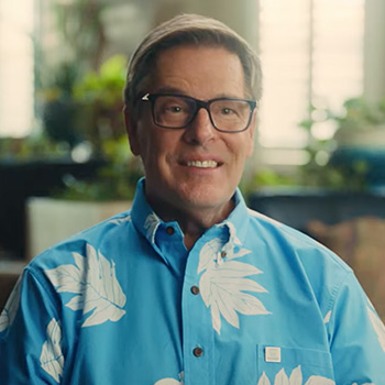 A one-quarter headshot of Burton Hughes, general manager of Subaru of Las Vegas. He is smiling and wearing a light-blue shirt with white leaf prints.