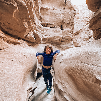 Everest Yasuda is standing between tall wind-swept rocks at Anza-Borrego Desert State Park. He’s resting an elbow on each formation, and other massive rocks surround him in the desert setting.