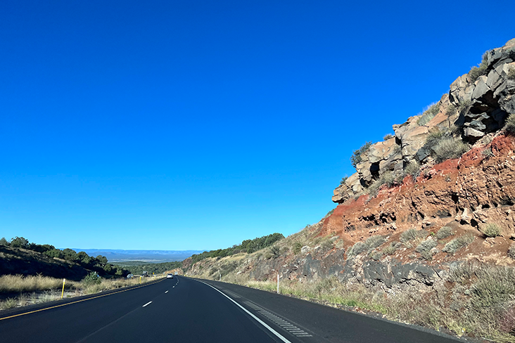 An image of the open road. There is an outcropping of rocky cliffs on the right and trees in the distance on the left.
