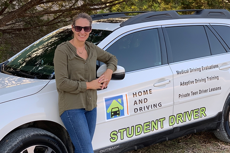 Megan Frazier smiling and looking relaxed as she leans on the driver’s side of her Subaru Outback. On the vehicle’s side it says, “Home and Driving; Student Driver; Medical Driving Evaluations; Adaptive Driving Training; and Private Teen Driver Lessons.”