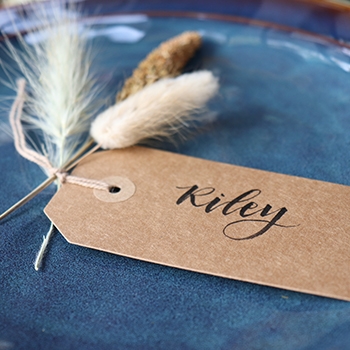 Closeup of a name tag that has “Riley” handwritten on it and is decorated with three ornamental grasses.