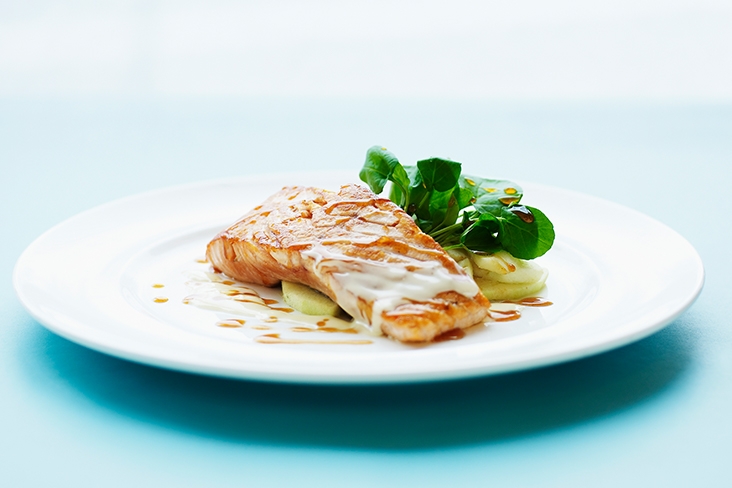 A single serving of beurre blanc plated artistically on a white plate sitting on a blue table.