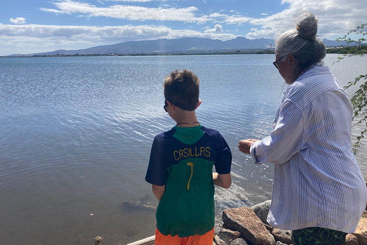 Nikko is standing at the water’s edge near the ancient fishpond with Aunty Kehau, a Native Hawaiian elder.