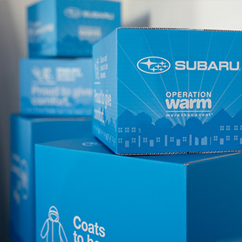 Several blue boxes stacked on top of each other that say Subaru and Operation Warm in white lettering