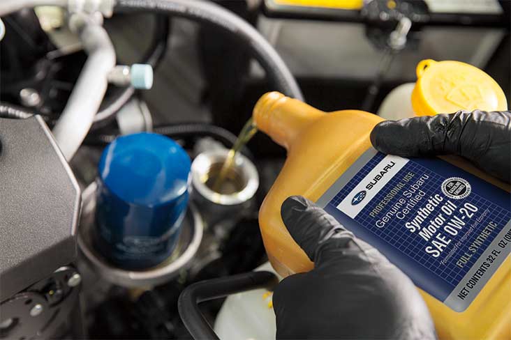 A closeup view of a bottle of Genuine Subaru Certified Synthetic Oil being poured into a vehicle’s engine.