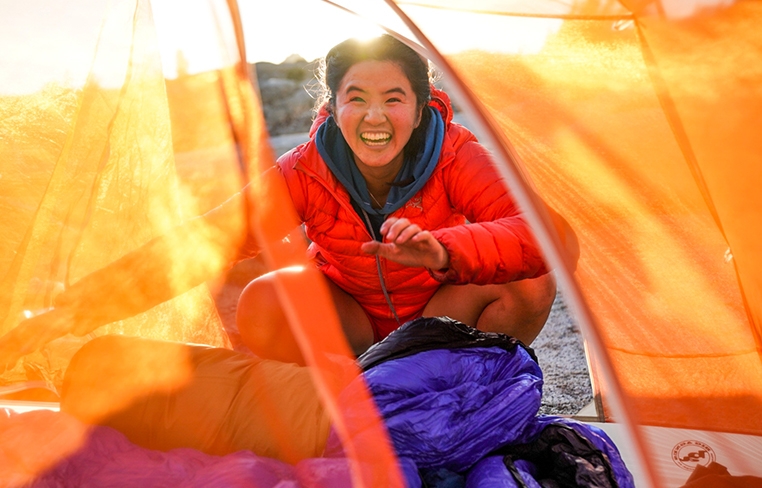 Dao peering into a tent with the sun shining brightly behind her