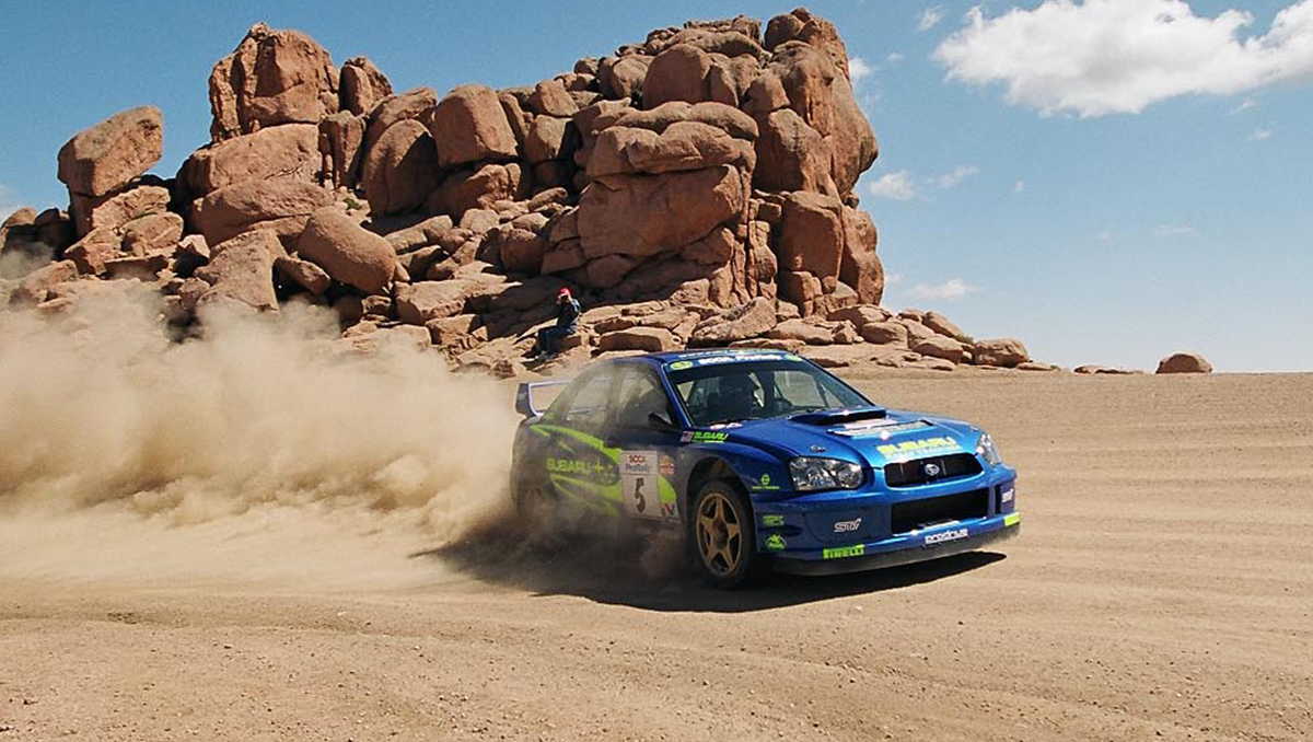 blue Subaru in front of rock formations 