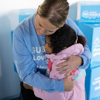 Close-up of a Subaru Loves to Help volunteer hugging a child who is wearing a brand-new pink jacket