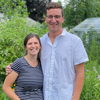 Katie and Karl Kloos in their yard with native plants and a greenhouse in the background.