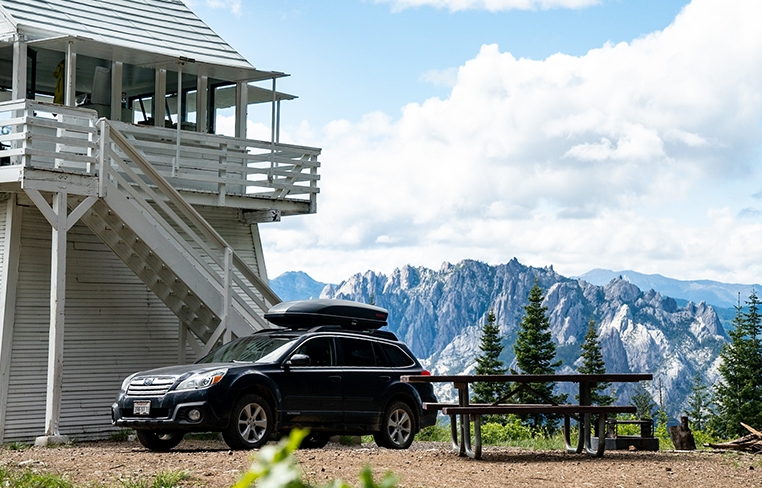 Dao’s Subaru Outback parked next to a lookout tower with mountains in the background.