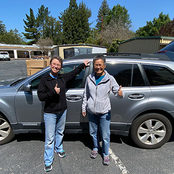 Wasko and Gilbert picking up a delivery at the warehouse with a silver Subaru Outback behind them