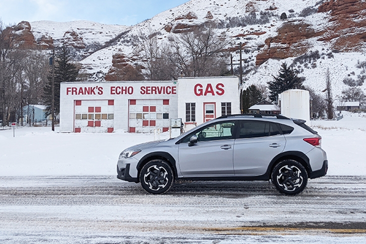 The writer’s Subaru Crosstrek is parked in front of Frank’s service station on a snowy road. The defunct structure is white and on the building it says, Frank’s Echo Service and Gas in red lettering. Beyond the service station are ragged brown outcroppings that are dusted with snow.