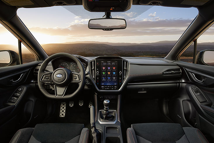 A cabin view inside the 2022 Subaru WRX from the perspective of the rear seat. Beyond the windshield are mountains and blue skies.