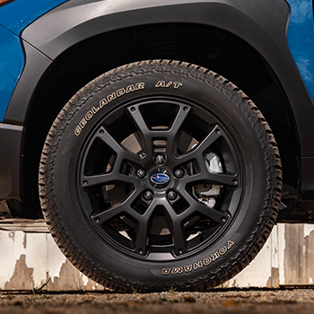 Closeup of a Subaru Crosstrek Wilderness Yokohama GEOLANDAR all-terrain tire and 17-inch alloy wheel in matte-black finish.